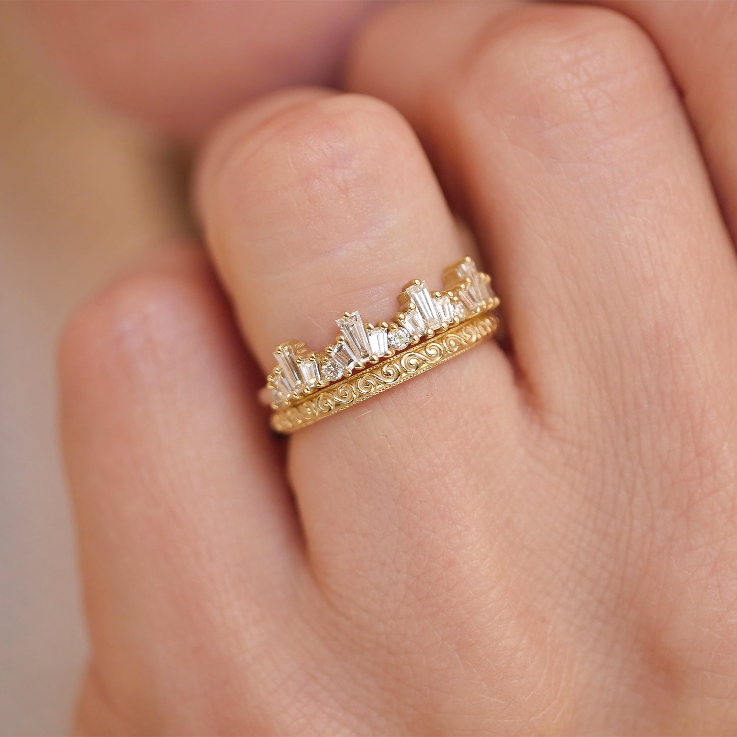 Woman wearing 14k yellow gold and baguette diamond tiara engagement ring stacked with a wind spiral wedding band.