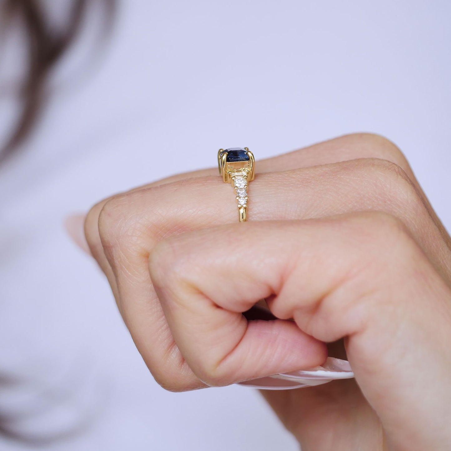 Gold ring with a blue gemstone on a person's finger against a neutral background