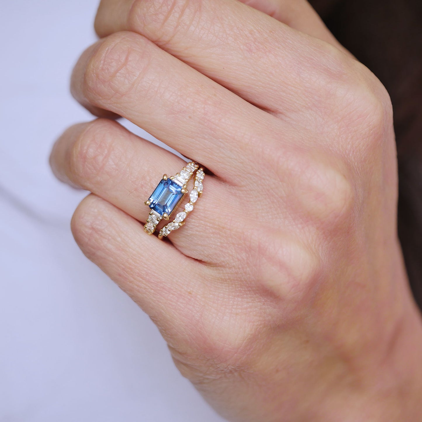 Hand wearing a ring with a blue gemstone and diamond accents on a plain background