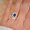 A woman wearing a blue sapphire and diamond cluster ring stacked with a cobblestone contour ring.
