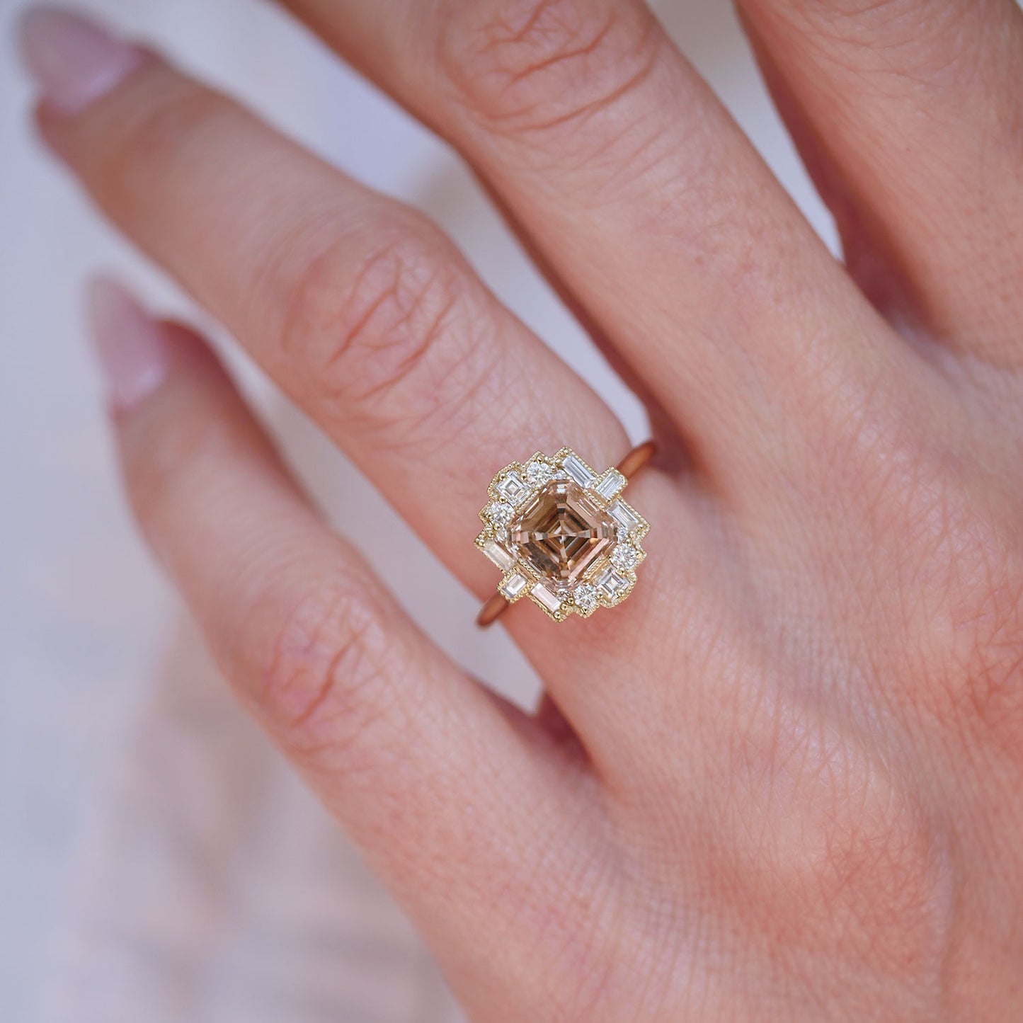 Close-up of a hand wearing a ring with white diamond and a champagne asscher center
