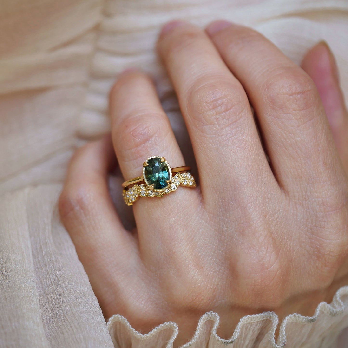 Close-up of a hand wearing a nature inspired gold band with a green sapphire engagement ring.