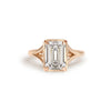 An emerald cut diamond solitaire ring with a rose gold band and milgrain detailing.