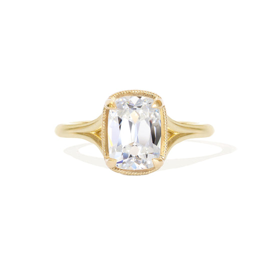 An elongated antique cushion cut solitaire ring with a lab-grown diamond and milgrain detailing on a yellow gold band.